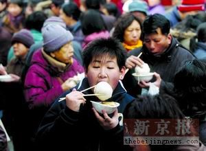 一位小孩端着碗站在人群中吃得津津有味.