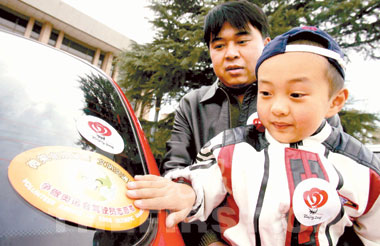 来自北京网通的驾驶员志愿者申请人肖力和他的儿子将志愿者文明交通车标贴在自己的车
