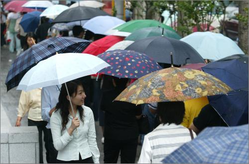 2007年5月24日,上海街头,撑着雨伞的市民在公交车站候车.