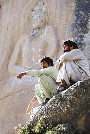 两名巴基斯坦青年正坐在被炸毁的佛像前面。