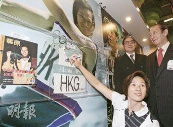 “风之后”李丽珊（前）极有可能成为香港奥运圣火传递的第一棒火炬手。她16日出席“香港金牌运动员成就展”时，在她1996年参加亚特兰大奥运夺金时所穿的奥运制服展品上签名。后为港协暨奥委会会长霍震霆。（图片来源：明报）