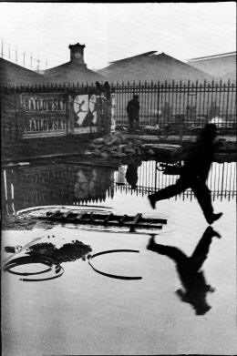 《圣·拉扎尔火车站》是布列松抓拍艺术的代表性作品，前景中跳跃的男子与背景招贴广告中的跳跃女郎相映成趣。