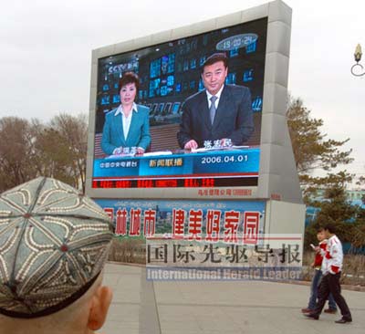 2006年4月1日，在乌鲁木齐人民广场上，一名维吾尔族市民正通过大型电子显示屏观看中央电视台《新闻联播》节目。本报资料图