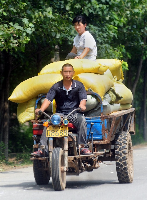 市境内的一条公路上,两位妇女同时坐在一辆货运机动三轮车的后挡板上