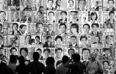 8月30日，在日本首都东京民主党众议院选举开票现场，记者们在贴有民主党议员候选人照片的海报墙前忙碌。