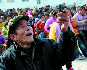 今年2月24日，移民姚百俊老人看到家乡来慰问的演出分外亲切，用手机拍下家乡戏。2009年8月，试点移民启动，淅川县共有1.08万试点移民迁入河南6个市。（资料图片）