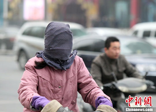 12月13日,河南郑州,寒风卷起马路上飘落的黄叶,民众蒙头,捂脸抵御,中