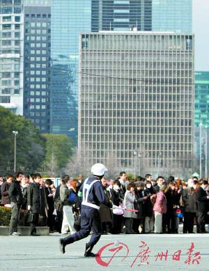 3月11日，在日本东京，一名警察跑过聚集在空旷地带避震的人群。 新华社发 