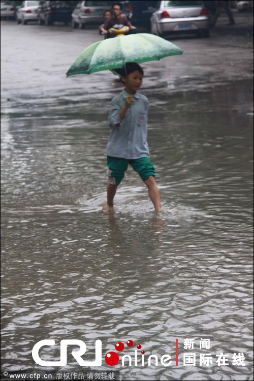 2011年6月5日,江西宜春持续暴雨,一名少年赤脚走在积水严重的潭前路.