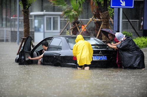 6月18日,一辆轿车在积水中熄火,行人帮忙推车.新华社记者郝同前摄