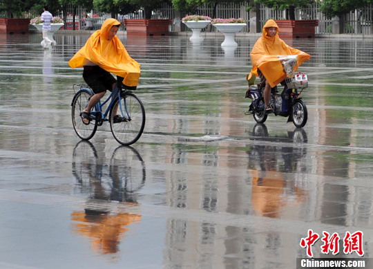 图为8月7日，苏州市昆山街头，披着雨披的市民冒雨骑车而行。泱波 摄