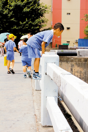 一名小学生正踩在护栏上往河面看.