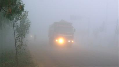 青岛北郊的218省道上大雾弥漫,能见度只有十几米,车辆在雾中开灯缓缓
