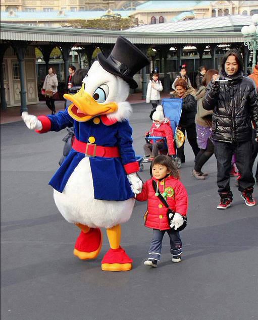 迪士尼乐园里牵着小女孩手走路的唐老鸭.