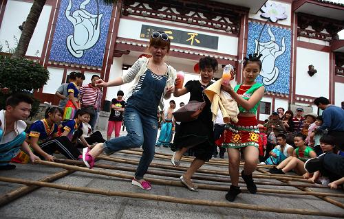 1月27日,游客和黎族姑娘在海南省三亚市南山佛教文化苑跳竹杆舞.