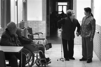 养老院的走廊内，一名老人拉着护工的手。