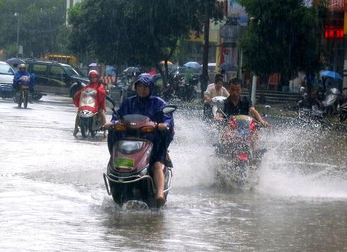 6月25日，在江西省于都县城长征大道，市民驾驶摩托车行进在积水的大街上。新华社发（康育生 摄）