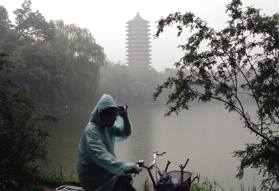 6月24日，一名学生披着雨衣骑过北大未名湖畔。24日至25日6时，北京迎来今年以来的最大一次降水。刘关关 摄