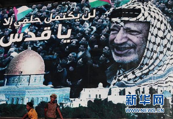 7月4日，在加沙城，巴勒斯坦人经过一张绘有巴勒斯坦民族权力机构前主席阿拉法特的巨幅海报。新华社发（纳赛尔摄）