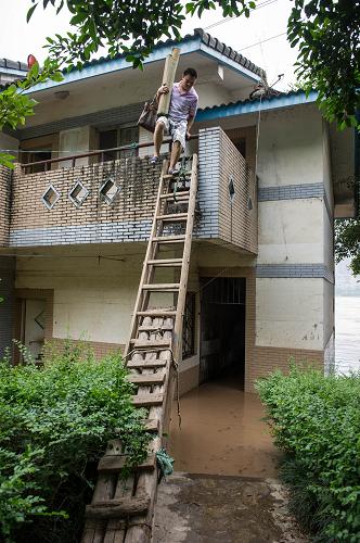 7月23日，由于洪水上涨太快，住在重庆市长滨路的市民只有搭梯子来抢运房间里的物品。新华社记者 陈诚 摄