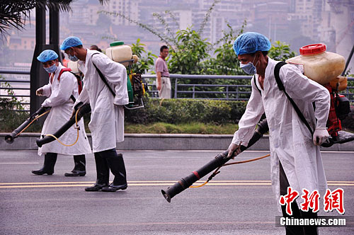 下午4时左右，31年来长江最大洪峰过境重庆主城后，水位有所回落，之前被淹的城市滨江路段露出水面。图为卫生防疫人员在退水路段喷洒消毒药水。李力摄