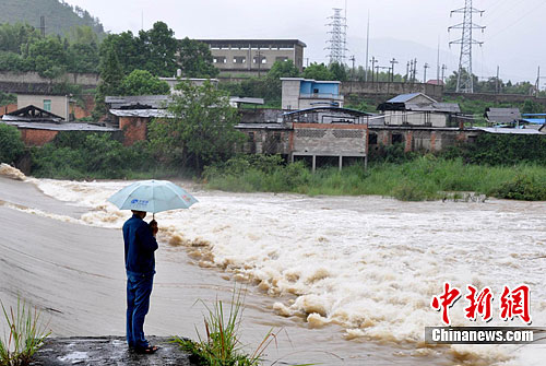 图为一人撑着伞看着滚滚洪水。胡敦煌摄