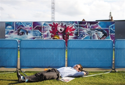 伦敦塔桥旁边的草坪上,躺着休息的人在看奥运会比赛直播.