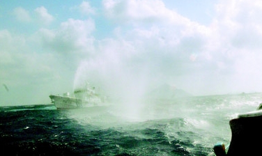 台湾南方澳渔船接近钓鱼岛（前方小岛）约3、4海里时，日本海上保安厅的巡逻船朝台湾渔船喷水驱赶。图片来源：台湾《联合报》