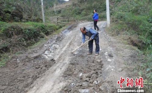 图为张朝富老人正在用锄头填坑修路.李胜成摄