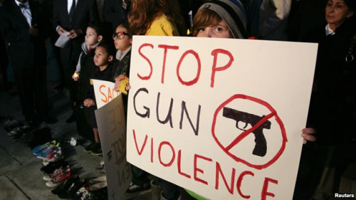19日在洛杉矶市政厅前举行的烛光守夜活动中，人们举着“制止枪击暴力”的标语牌。