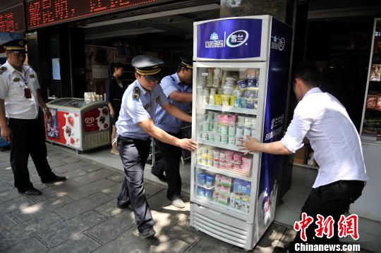 图为昆明城管执法人员与店主一起将占道冰箱抬进店内。 刘冉阳 摄