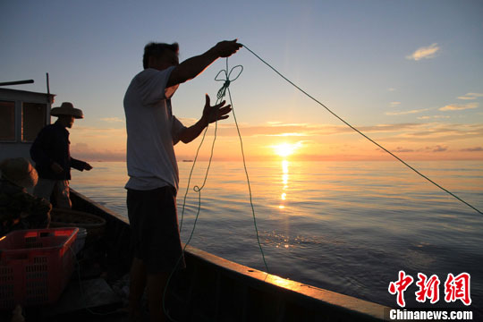 5月14日下午,在海南赴南沙捕捞船队抛锚海区,渔民在夕阳中放线钓鱼.