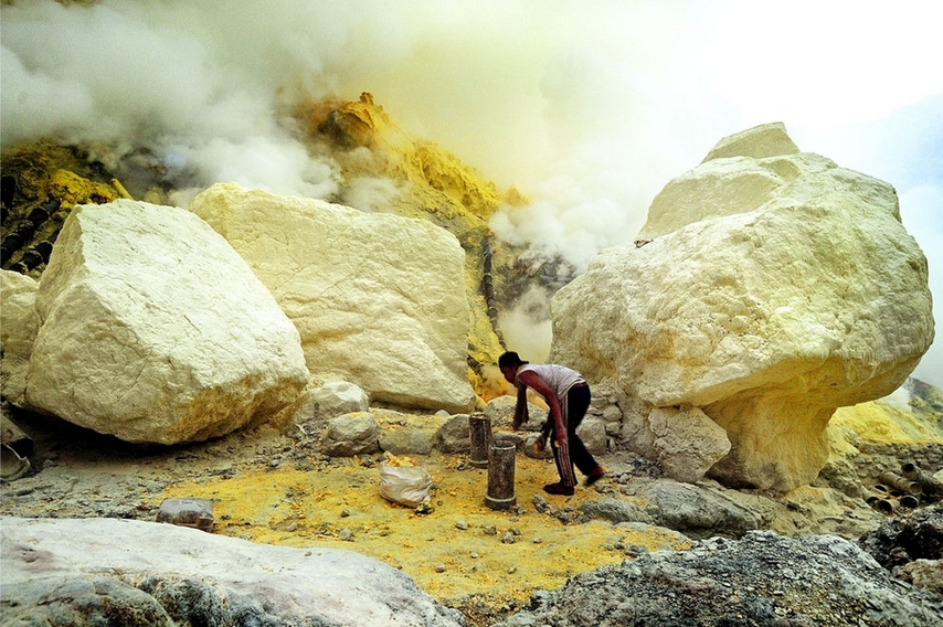 一位矿工辛勤地挖着硫磺块,忍受着高温气体.图片