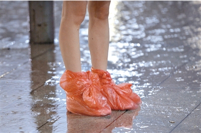 五棵松篮球馆旁,一个女孩脚上套着塑料袋站在雨中.