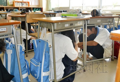 7月5日上午，日本石川县举行地震防灾演练，金泽市的初中生听到校内广播后一齐躲到桌下。（共同社）