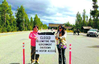 因美国政府关闭导致全美国家公园关闭，有中国游客1日在黄石公园遭遇闭门羹，举着关门牌子表示抗议。（美国《世界日报》）