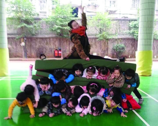 長沙師范學院附屬第一幼兒園的家長聯系QQ群里，出現了這么一張照片:由墊子隔開，上下三排孩子，最上面還壓著一女老師，秀著一字馬。