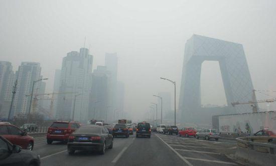 2月21日,车辆行驶在雾霾笼罩的北京街头,中央电视台新址大楼依稀可见。