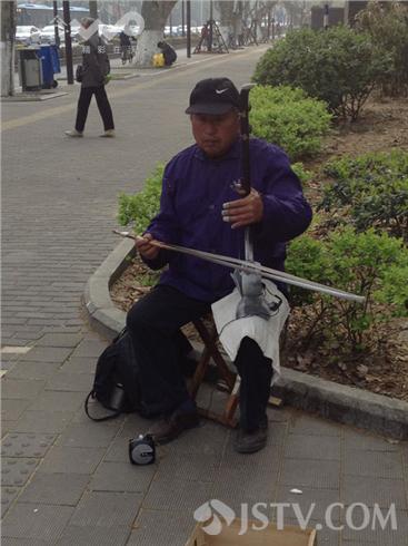 两名街头卖艺人,一人拉着二胡,另一人穿着红色戏服,挂着胡须,最主要画