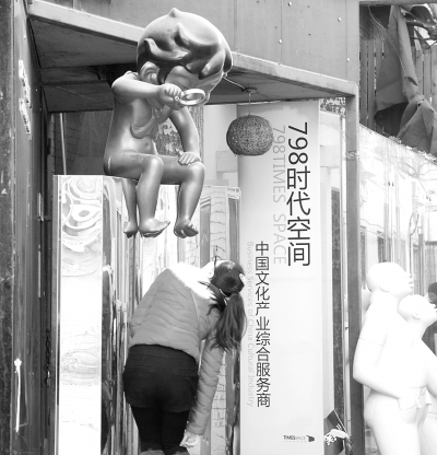 北京798艺术区，雕塑上的孩子用放大镜审视着眼前的美女。CFP