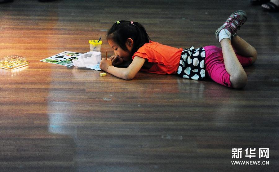 6月14日,一名小朋友趴在地上用颜料在帽子上画画.