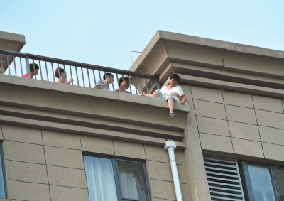 轻生女子坐在楼顶护栏外，多人正在进行劝说。京华时报记者赵思衡摄