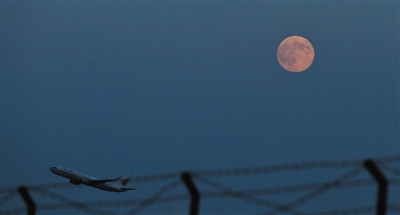 机场附近，一架飞机从月亮下飞过。新京报记者 薛珺 摄
