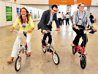 9日，三名与会人员在会场内试骑磁动车（一种新能源电动车）。今年的夏季达沃斯论坛提出“绿色”理念。新华社记者 岳月伟 摄