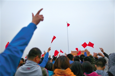 国旗升至旗杆顶部，迎风飘扬。广场上的人们向着国旗挥手。新京报记者浦峰摄