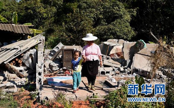 12月6日晚，云南省景谷县永平镇群众推车经过一栋被地震震裂的房屋。 新华社记者 蔺以光