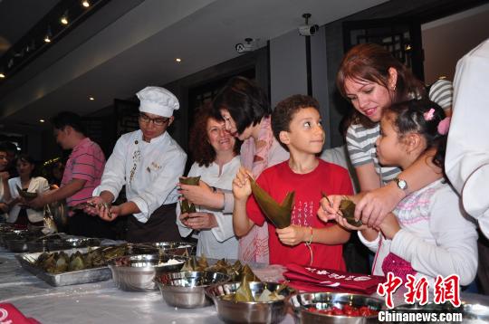 北京市政府新闻办主任、北京冬奥申委副秘书长王惠（左）女士19日晚与来自古巴的拉美通讯社记者的7岁女儿萨尔玛一起包粽子。 张雁晴 摄