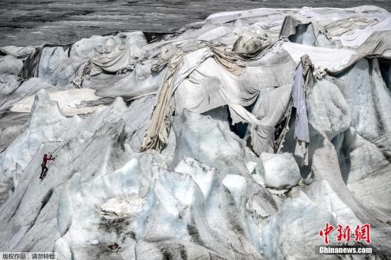 资料图：7月14日，在瑞士阿尔卑斯山脉的罗纳冰川，一名女子在保护冰川的隔热材料附近进行冰上攀岩。瑞士罗纳冰川位于瑞士瓦莱州。瑞士壮美的冰川景观吸引着世界各地游客。受全球气候变暖影响，瑞士冰川不断消融。