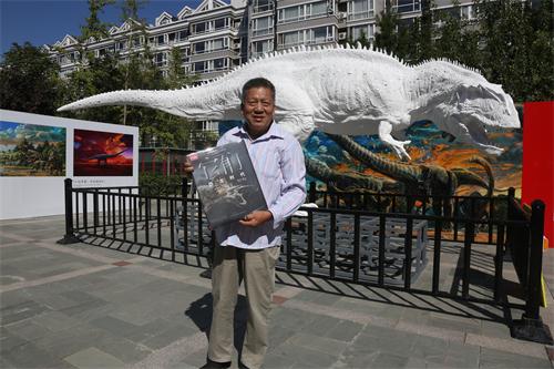 (一位恐龙资深粉丝在永川龙雕像前展示《它们:恐龙时代》图书)