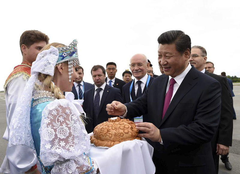 图为：7月8日，国家主席习近平乘坐专机抵达乌法，应俄罗斯联邦总统普京邀请，出席金砖国家领导人第七次会晤和上海合作组织成员国元首理事会第十五次会议。这是在乌法国际机场，身穿俄罗斯民族服饰的青年按当地迎接贵宾的传统，向习近平敬献面包和盐。习近平掰下一小块面包，蘸盐品尝。